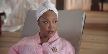 Movie still from “Vacation Friends” (2021), directed by Clay Tarver – An older woman wearing a white head scarf; Close Up shot, Over the shoulder angle
