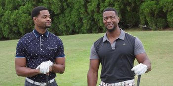 Movie still from “Vacation Friends” (2021), directed by Clay Tarver – A couple of men standing on top of a grass covered field; Medium shot, Over the shoulder angle