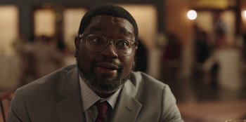 Movie still from “Vacation Friends” (2021), directed by Clay Tarver – A person wearing a suit and glasses; Close Up shot, Over the shoulder angle