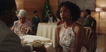 Movie still from “Vacation Friends” (2021), directed by Clay Tarver – A woman sitting at a table with a plate of food in front of her; Medium shot, Over the shoulder angle