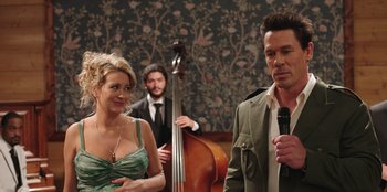 Movie still from “Vacation Friends” (2021), directed by Clay Tarver – A man and a woman standing next to a man holding a microphone; Medium shot, Over the shoulder angle