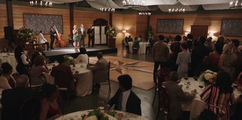 Movie still from “Vacation Friends” (2021), directed by Clay Tarver – A group of people sitting at tables in front of a stage; Extreme Wide shot, High angle