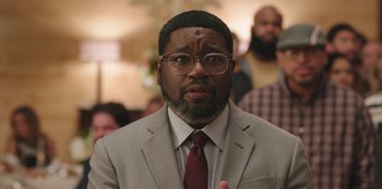 Movie still from “Vacation Friends” (2021), directed by Clay Tarver – A person wearing a suit and glasses; Close Up shot, Over the shoulder angle