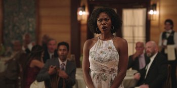 Movie still from “Vacation Friends” (2021), directed by Clay Tarver – A woman standing in front of a man in front of a table; Medium shot, Over the shoulder angle