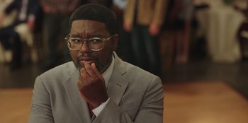 Movie still from “Vacation Friends” (2021), directed by Clay Tarver – A man in a gray suit and red tie; Close Up shot, Over the shoulder angle