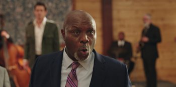 Movie still from “Vacation Friends” (2021), directed by Clay Tarver – A man in a suit and tie making a funny face; Close Up shot, Low angle