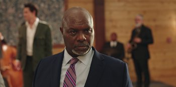 Movie still from “Vacation Friends” (2021), directed by Clay Tarver – A man in a suit and tie looking at the camera; Close Up shot, Low angle