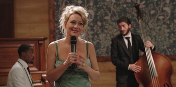 Movie still from “Vacation Friends” (2021), directed by Clay Tarver – A woman holding a microphone in front of a man in a suit; Medium shot, Over the shoulder angle