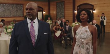 Movie still from “Vacation Friends” (2021), directed by Clay Tarver – A man and a woman standing next to each other in front of a group of people; Medium shot, Over the shoulder angle