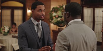 Movie still from “Vacation Friends” (2021), directed by Clay Tarver – A man in a gray suit talking to another man in a gray suit; Medium shot, Over the shoulder angle