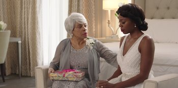 Movie still from “Vacation Friends” (2021), directed by Clay Tarver – An older woman holding a gift box while a younger woman looks on; Medium shot, Over the shoulder angle