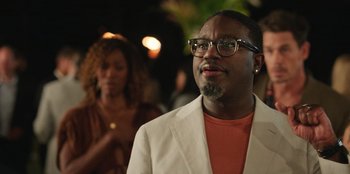 Movie still from “Vacation Friends 2” (2023), directed by Clay Tarver – A man with glasses and a beard wearing a white jacket; Close Up shot, Over the shoulder angle