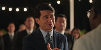 Movie still from “Vacation Friends 2” (2023), directed by Clay Tarver – A man in a suit and tie claps his hands; Close Up shot, Over the shoulder angle