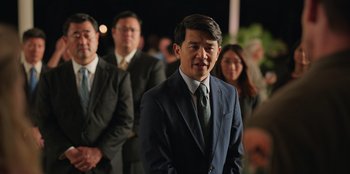 Movie still from “Vacation Friends 2” (2023), directed by Clay Tarver – A man in a suit standing in front of a group of people; Medium shot, Over the shoulder angle