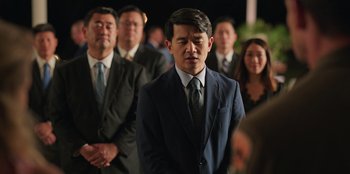 Movie still from “Vacation Friends 2” (2023), directed by Clay Tarver – A group of people standing around a man in a suit and tie; Medium shot, Over the shoulder angle