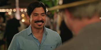 Movie still from “Vacation Friends 2” (2023), directed by Clay Tarver – A man with a mustache smiling for the camera; Close Up shot, Over the shoulder angle