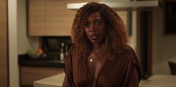 Movie still from “Vacation Friends 2” (2023), directed by Clay Tarver – A woman in a brown dress is standing in a kitchen; Close Up shot, Over the shoulder angle