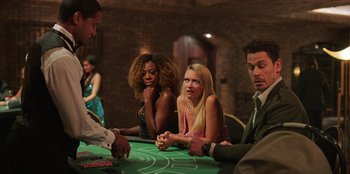 Movie still from “Vacation Friends 2” (2023), directed by Clay Tarver – A group of people sitting around a table playing blackjack; Medium shot, High angle