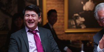 Movie still from “Vacation Friends 2” (2023), directed by Clay Tarver – A man in a suit and a tie laughing; Close Up shot, Over the shoulder angle