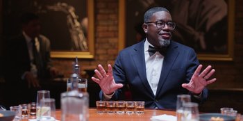 Movie still from “Vacation Friends 2” (2023), directed by Clay Tarver – A man sitting at a table in front of a row of shots; Medium shot, Over the shoulder angle