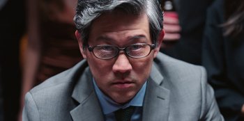 Movie still from “Vacation Friends 2” (2023), directed by Clay Tarver – A person wearing a suit and glasses; Close Up shot, Over the shoulder angle