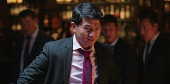 Movie still from “Vacation Friends 2” (2023), directed by Clay Tarver – A man in a suit and tie standing in front of other men; Close Up shot, Low angle