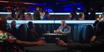 Movie still from “Vacation Friends 2” (2023), directed by Clay Tarver – A group of men sitting at a booth in a bar; Wide shot, Over the shoulder angle