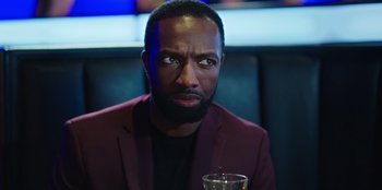 Movie still from “Vacation Friends 2” (2023), directed by Clay Tarver – A man in a red jacket is holding a glass; Close Up shot, Over the shoulder angle