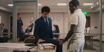 Movie still from “Vacation Friends 2” (2023), directed by Clay Tarver – A man in a suit and tie holding a box; Medium shot, Over the shoulder angle