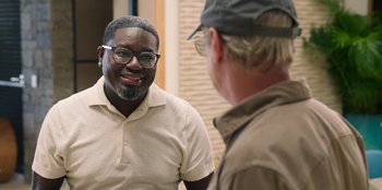 Movie still from “Vacation Friends 2” (2023), directed by Clay Tarver – A man wearing glasses talking to another man wearing a hat; Medium shot, Over the shoulder angle