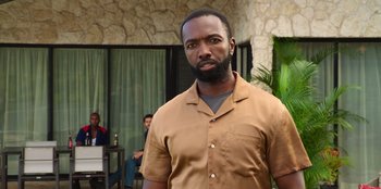 Movie still from “Vacation Friends 2” (2023), directed by Clay Tarver – A man in a brown shirt is standing in front of a building; Medium shot, Over the shoulder angle