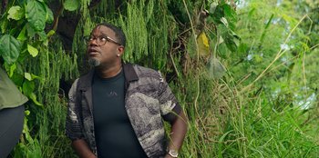 Movie still from “Vacation Friends 2” (2023), directed by Clay Tarver – A man standing in front of a tree with his hands in his pockets; Medium shot, Low angle