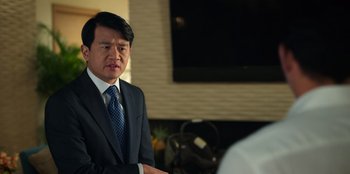 Movie still from “Vacation Friends 2” (2023), directed by Clay Tarver – A man wearing a suit and tie in front of a television; Close Up shot, Over the shoulder angle