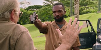 Movie still from “Vacation Friends 2” (2023), directed by Clay Tarver – A man holding up a cell phone in front of another man; Medium shot, Over the shoulder angle