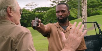 Movie still from “Vacation Friends 2” (2023), directed by Clay Tarver – A man holding a cell phone up to the camera; Medium shot, Over the shoulder angle