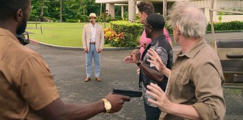 Movie still from “Vacation Friends 2” (2023), directed by Clay Tarver – A group of people standing in a parking lot holding guns; Wide shot, Over the shoulder angle