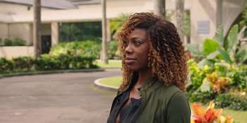 Movie still from “Vacation Friends 2” (2023), directed by Clay Tarver – A woman standing in front of a building with long curly hair; Close Up shot, Over the shoulder angle