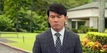 Movie still from “Vacation Friends 2” (2023), directed by Clay Tarver – A man wearing a suit and tie standing in front of a house; Close Up shot, Over the shoulder angle