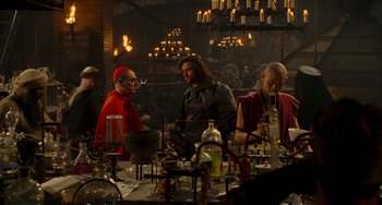 Movie still from “Van Helsing” (2004), directed by Stephen Sommers – A group of people standing around a table with bottles; Medium shot, Over the shoulder angle