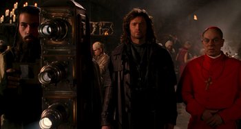 Movie still from “Van Helsing” (2004), directed by Stephen Sommers – A man with long curly hair standing next to an oven; Medium shot, Over the shoulder angle