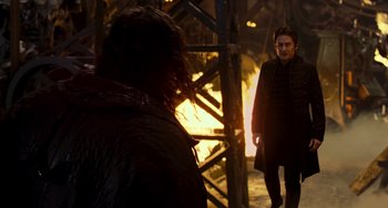 Movie still from “Van Helsing” (2004), directed by Stephen Sommers – A man standing next to another man in front of a fire pit; Medium shot, Over the shoulder angle