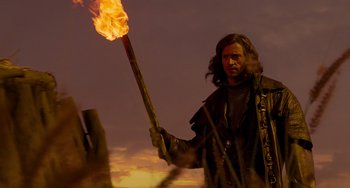 Movie still from “Van Helsing” (2004), directed by Stephen Sommers – A man holding up a burning torch in front of a sky background; Medium shot, Low angle