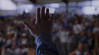 Movie still from “Varsity Blues” (1999), directed by Brian Robbins – A person with a ring on their finger is raising their hand in front of an audience; Extreme Close Up shot, Over the shoulder angle