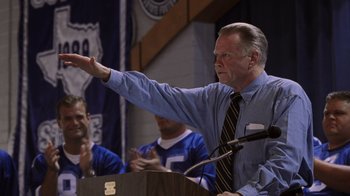 Movie still from “Varsity Blues” (1999), directed by Brian Robbins – An older man giving a speech at a podium; Medium shot, Over the shoulder angle