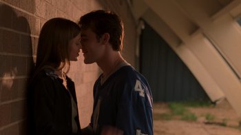 Movie still from “Varsity Blues” (1999), directed by Brian Robbins – A man and a woman kissing in front of a brick wall; Medium shot, Low angle