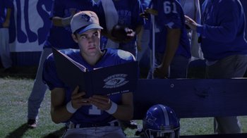 Movie still from “Varsity Blues” (1999), directed by Brian Robbins – A football player reading a book while sitting on the sidelines; Close Up shot, Over the shoulder angle