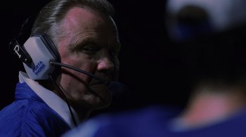 Movie still from “Varsity Blues” (1999), directed by Brian Robbins – An older man with a microphone in his ear; Close Up shot, Low angle
