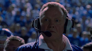 Movie still from “Varsity Blues” (1999), directed by Brian Robbins – An older man wearing a headset in front of an audience; Close Up shot, Low angle