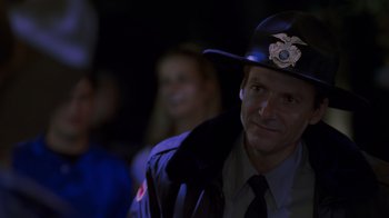 Movie still from “Varsity Blues” (1999), directed by Brian Robbins – A man in a police uniform is smiling for the camera; Close Up shot, Over the shoulder angle