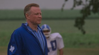 Movie still from “Varsity Blues” (1999), directed by Brian Robbins – An older man in a blue jacket is standing in front of a football player; Medium shot, Low angle